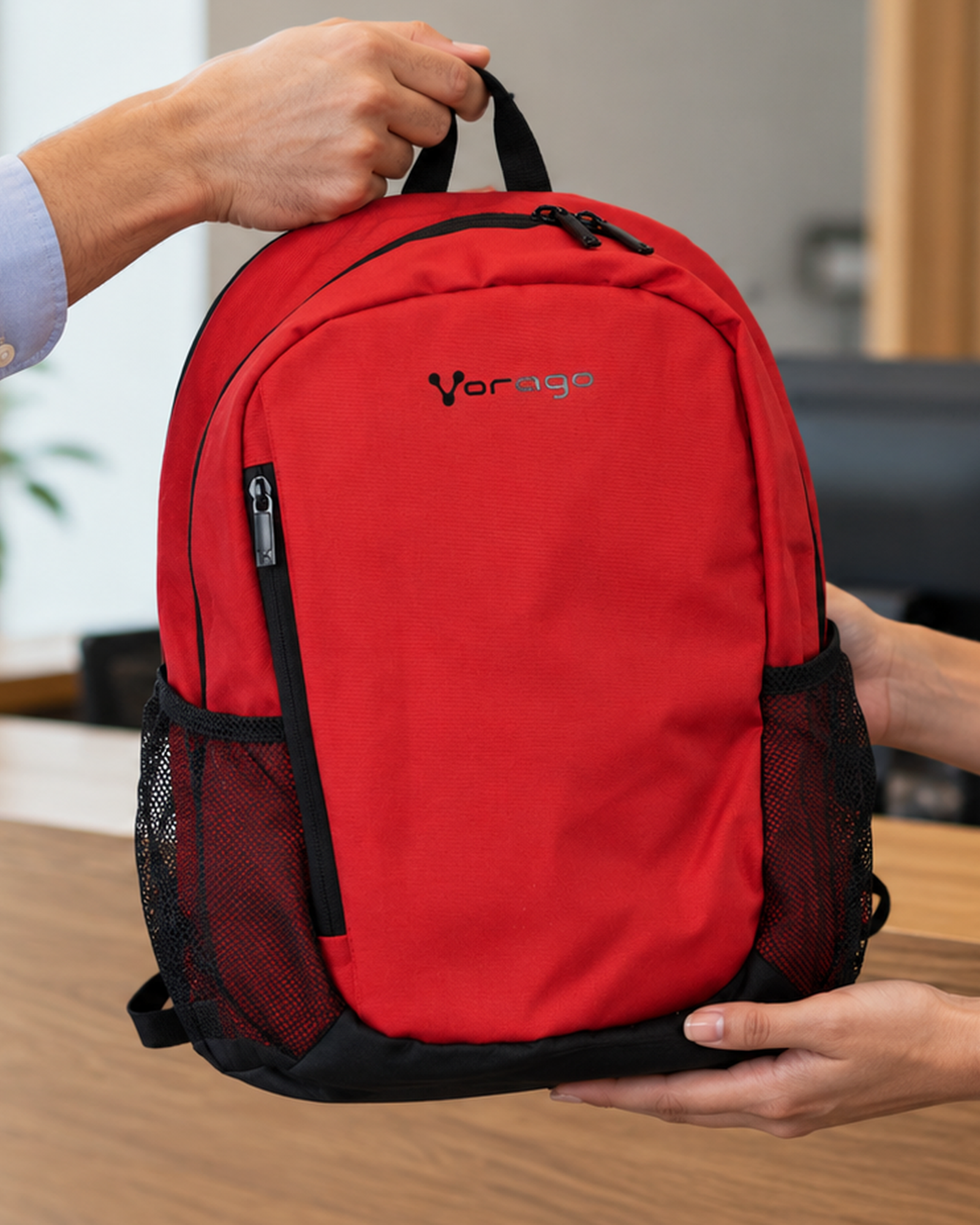 Un ejecutivo entrega a su cliente una mochila VORAGO BP-150 roja tomándola del asa.